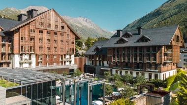 Vista esterna dell'hotel in stile chalet con piscina in primo piano e montagne sullo sfondo