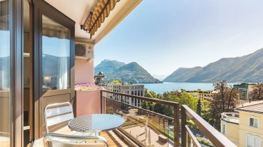 Balkon mit zwei Stühlen und einem Tisch, welcher eine See und Berglandschaft überblickt.