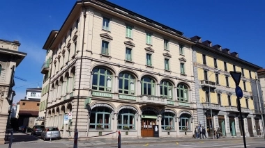 Städtisches Gebäude mit weiss-beiger Fassade und pastelgrünen Fenstern.