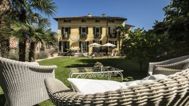 Giardino mediterraneo con mobili da salotto in primo piano e una villa gialla sullo sfondo.