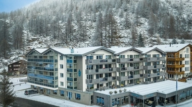 Buildings with balconies in front of a snow-covered hill.