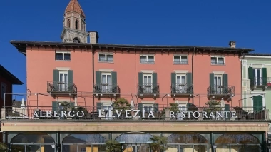 Exterior shot of the hotel with pink façade in sunny weather, with church tower in the background.