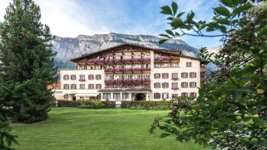 Blick auf das Hotel, den weitläufigen Park und die verschneiten Berge im Hintergrund.