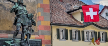 A statue in front of a historic building, next to a Swiss flag.