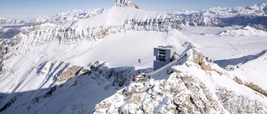 Eine verschneite Berglandschaft mit einem modernen Gebäude und einer Gruppe Menschen auf dem Gipfel.