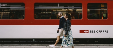 Two people walk past a red SBB train.