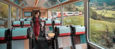 A woman walks through an empty panoramic train with large windows offering a view of the landscape.