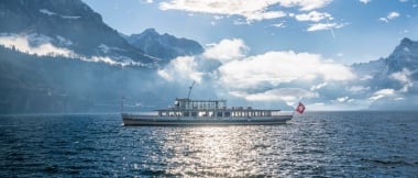 A ship on a lake, surrounded by mountains under a bright sun.