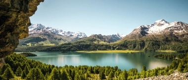 A tranquil mountain landscape with a lake, surrounded by forests and snow-capped peaks.