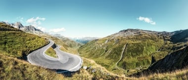 Strada di montagna ventosa in un paesaggio collinare verde sotto un cielo chiaro e blu.