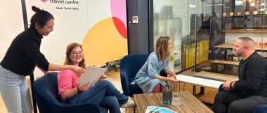 Eine Gruppe von vier Personen sitzt in einem modernen Büro zusammen und schaut in einen Katalog.