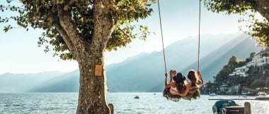 Two women sit on a swing and look out over the lake