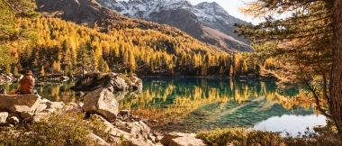Eine Frau sitzt am idyllischen Bergsee umgeben von herbstlichen Bäumen