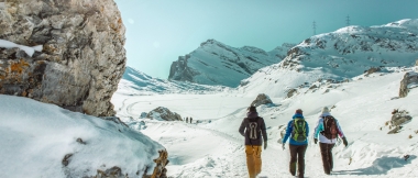 Tre escursionisti invernali in un paesaggio montano innevato sotto un cielo blu.