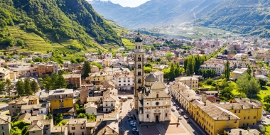 A beautiful Italian town surrounded by green hills and mountains, with a distinctive church in the center.