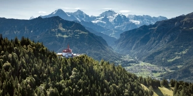 A mountain landscape with a red tower top, surrounded by dense forests and majestic snowy peaks in the background.