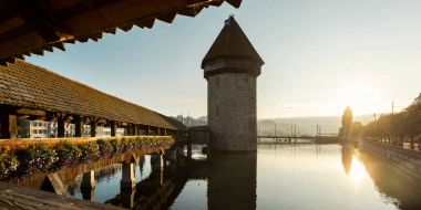 Un vecchio ponte di legno con fiori, accanto a una torre dell'acqua al sole della sera.