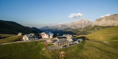 Una stazione di montagna con edifici, parcheggio e montagne sullo sfondo sotto un cielo sereno.