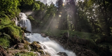 Wasserfall in einem grünen Wald mit Sonnenstrahlen durch Bäume.