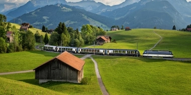 A train ride through a green hilly landscape with mountains in the background.