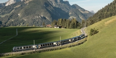 Train passes through green hills in front of a mountainous landscape.