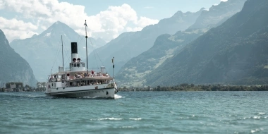 Ein Dampfschiff auf einem See mit Bergen im Hintergrund.