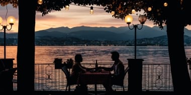 Two people sitting at a table by the lakeside at sunset.