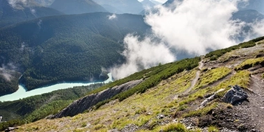 A mountain landscape with a green valley, cloud-covered hills, and a turquoise river.