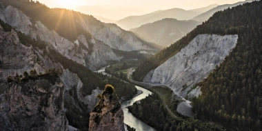 Sunset over a mountain gorge with a river and wooded slopes.