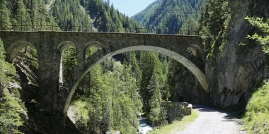 A stone railway bridge spans a wooded gorge with a stream below.