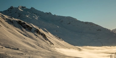 Un paysage de montagne enneigé sous un ciel dégagé, avec du brouillard dans la vallée.