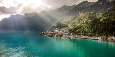 An idyllic mountain landscape with a tranquil lake and a small village on the shore under a dramatic sky.