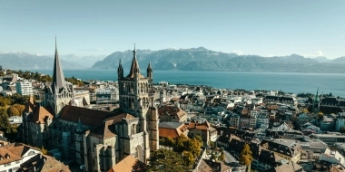 Aerial view of a historic church in a town with a lake and mountains in the background.