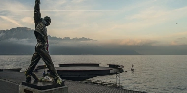 A statue on a pier by the lake with mountains in the background at sunset.