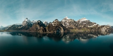 Expansive mountain landscape with snow-covered peaks and a tranquil lake in the foreground.