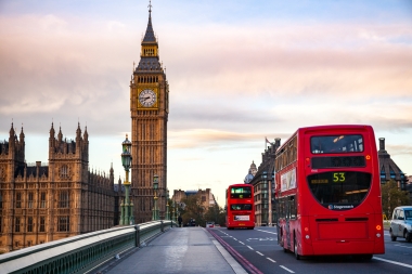 Eine Londoner Strasse bei Sonnenuntergang mit Big Ben und roten Doppeldeckerbussen.