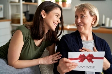 Zwei Frauen lachen, während eine von ihnen einen Geschenkgutschein hält.