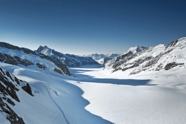 Eine weite verschneite Gebirgslandschaft unter klarem blauem Himmel.