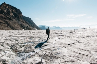 Un escursionista su un ghiacciaio soleggiato con montagne sullo sfondo.