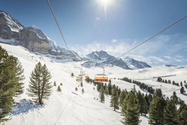 A ski lift cable car passes over a snow-covered landscape with mountains in the background.