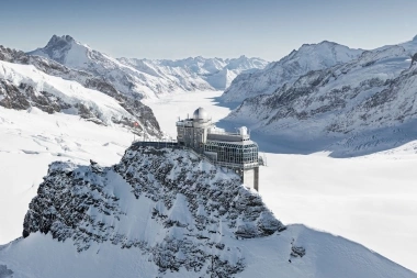 Observatorium auf verschneitem Berg mit atemberaubender Alpenlandschaft im Hintergrund.