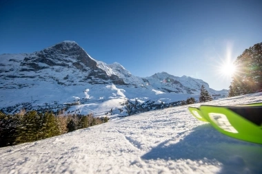 Eine verschneite Berglandschaft unter strahlend blauem Himmel mit Sonne im Hintergrund.