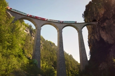 Ein roter Panoramazug überquert das beeindruckende Landwasserviadukt, ein ikonisches Bauwerk, eingebettet in eine grüne Berglandschaft.