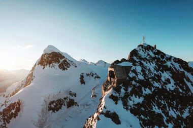 Eine Seilbahnstation auf einem verschneiten Berggipfel bei Sonnenaufgang.