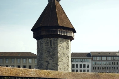 Tower and covered bridge with flowers over a river.