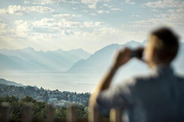 A person photographing a landscape with mountains and a lake in the background.