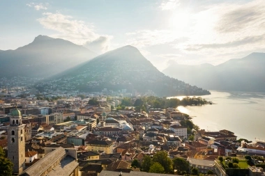 A city by the lake, surrounded by mountains in sunlight.