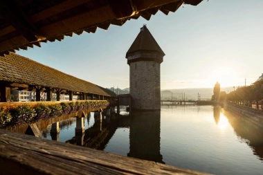 Un vecchio ponte di legno con fiori, accanto a una torre dell'acqua al sole della sera.