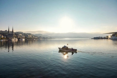 Eine ruhige Seelandschaft mit einem Boot im Vordergrund und einer Stadt im Hintergrund bei Sonnenuntergang.