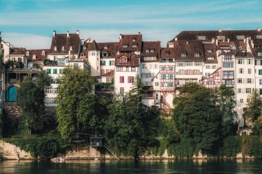 A row of historic half-timbered houses surrounded by trees on a riverbank.